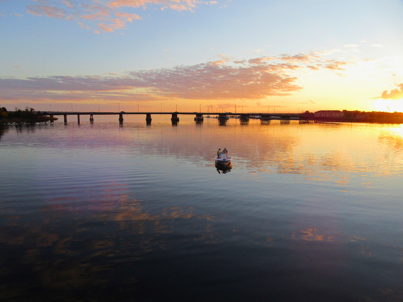 Boat on a lake with a bridge and sunset in the background