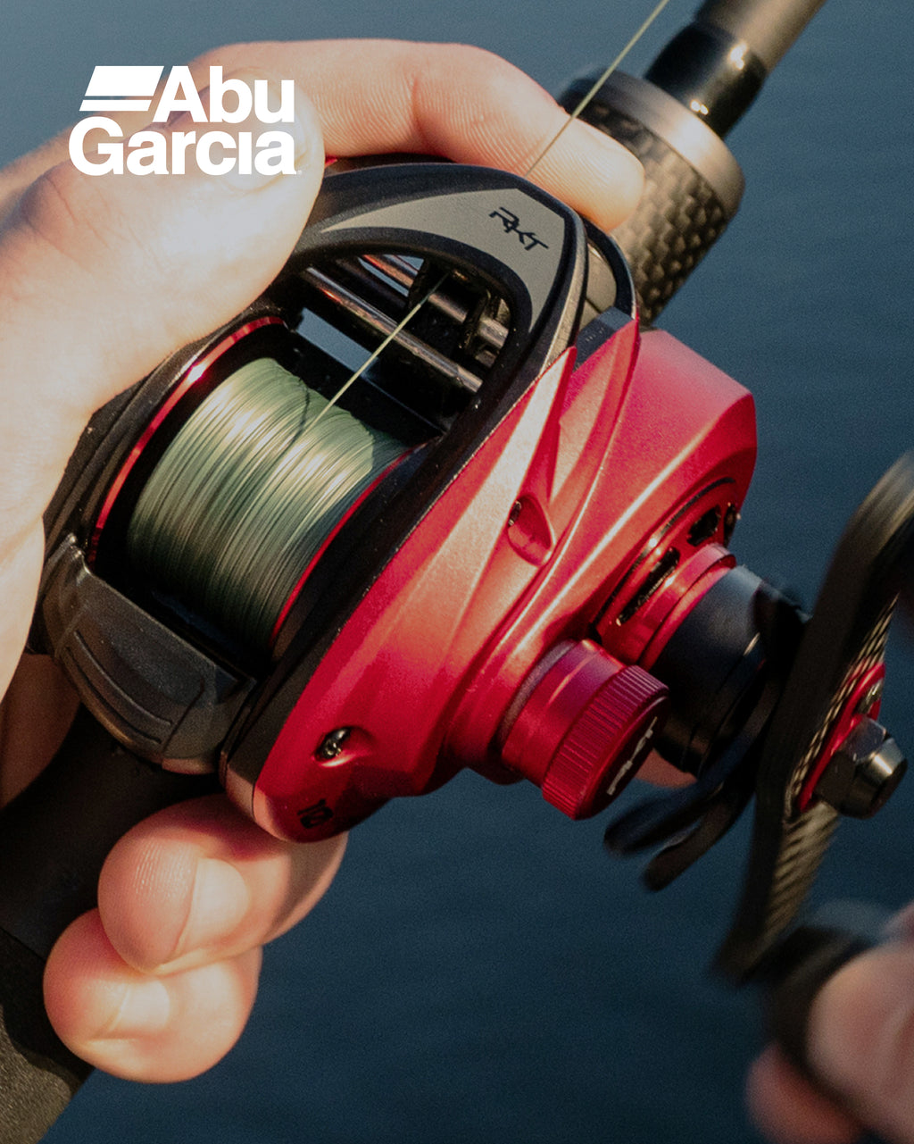 Red Abu Garcia fishing reel held by a person with water in the background