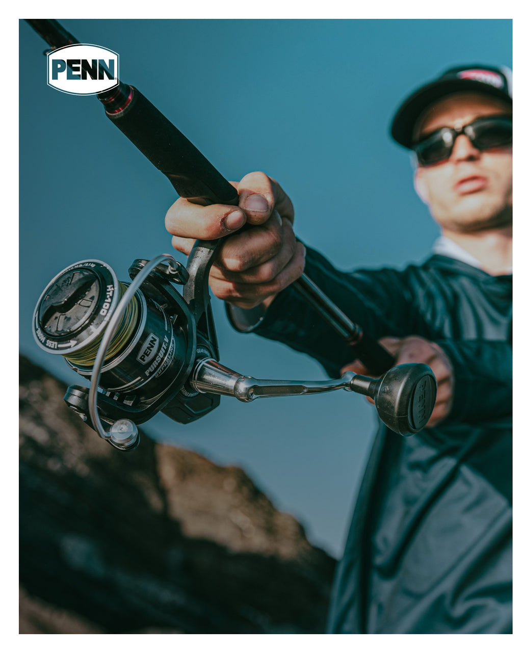 Person holding a fishing rod with a Penn reel against a blue sky.